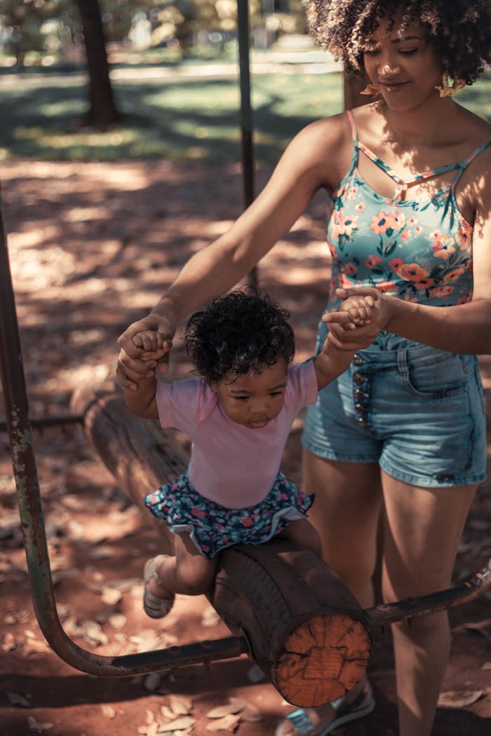 A joyful moment of a mother assisting her daughter on a log in a sunny park, depicting family bonding and fun.