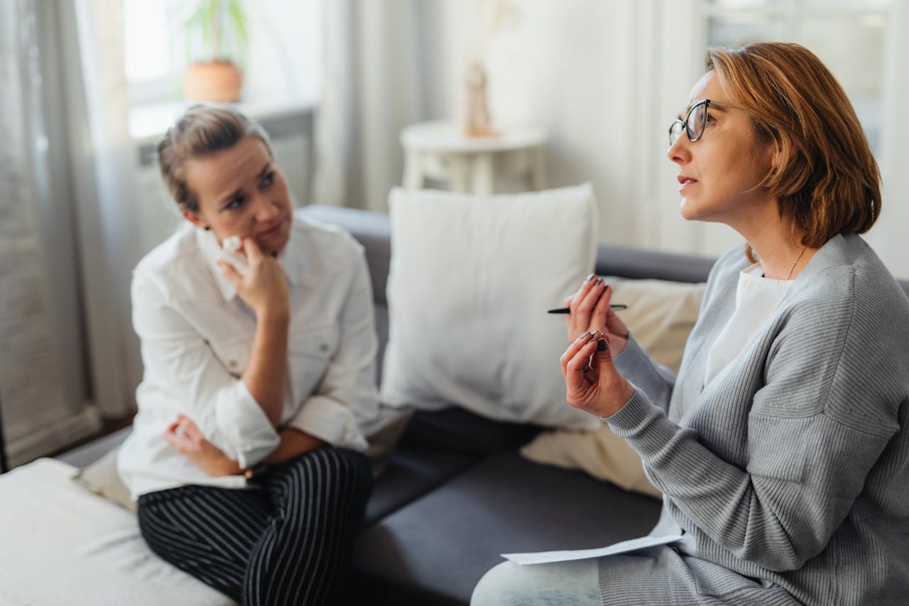 Two women engaged in a thoughtful counseling session in a cozy indoor setting.