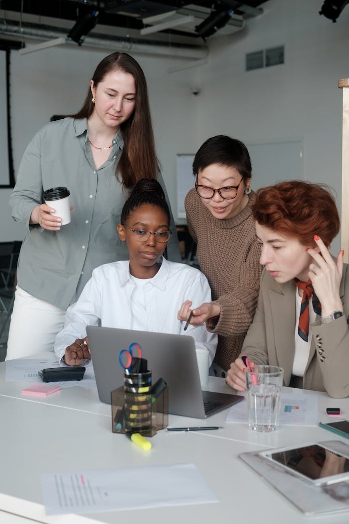 A diverse group of women working together at a laptop in an office setting.